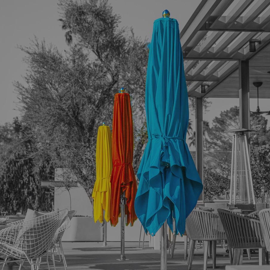 Yellow, orange, and teal patio umbrellas in color against a black-and-white desert courtyard